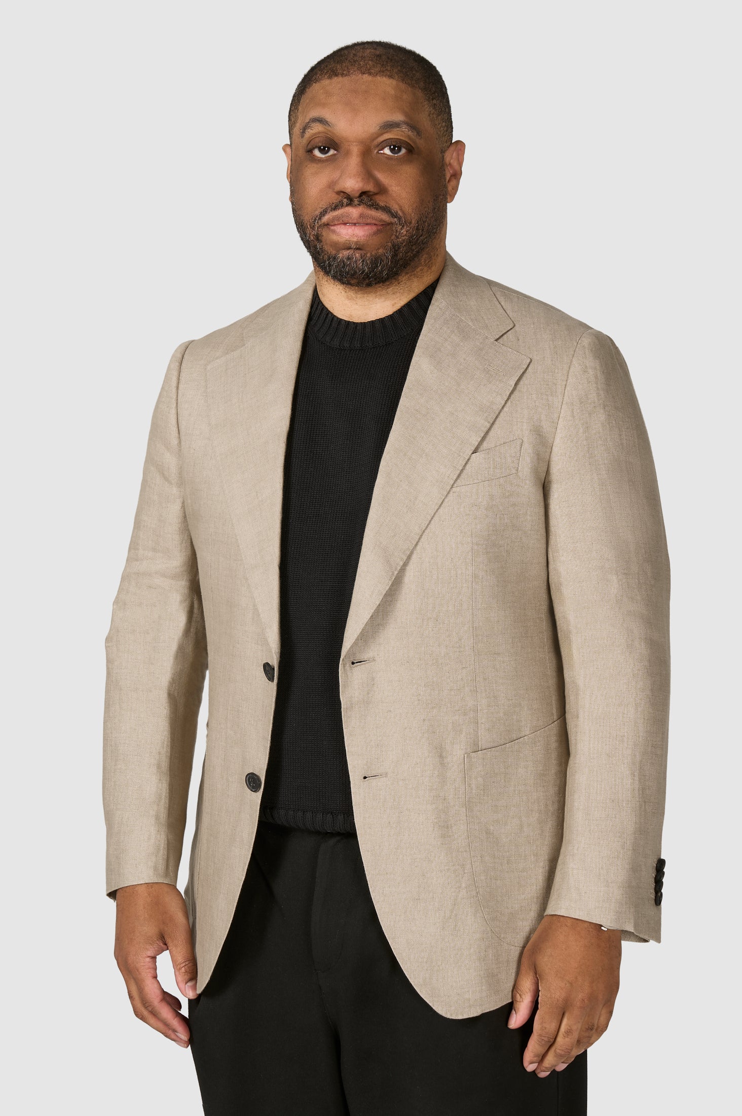 Man wearing a beige blazer over a black shirt on a white background